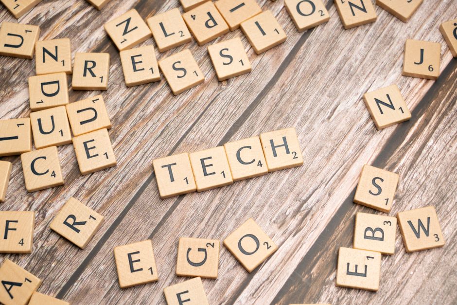 Wooden Scrabble tiles spelling TECH on a textured surface, showcasing creativity