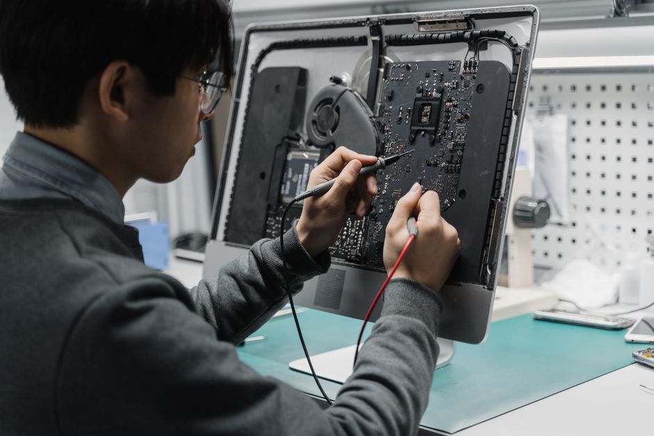 A technician works on a computer motherboard using tools at a workspace